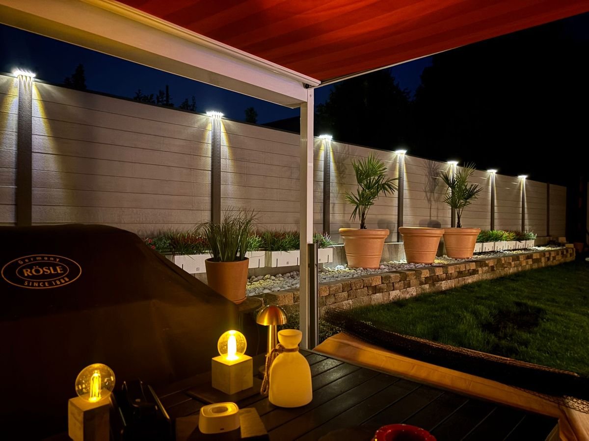 Überdachte Terrasse mit Zaunbeleuchtung bei Nacht – Außenanlage von STERKALAND Lübeck